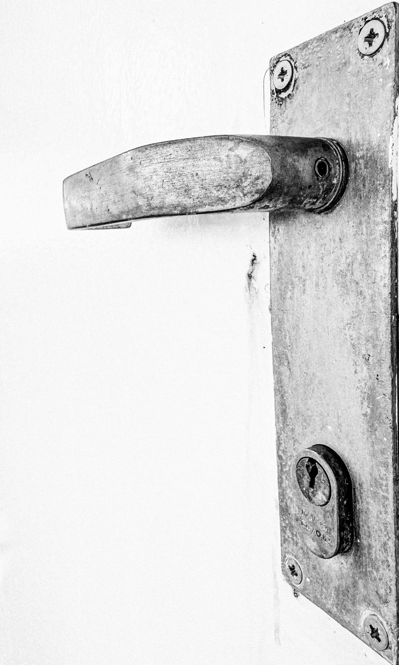 a black and white photo of an old metal door handle and lock plate against a white door