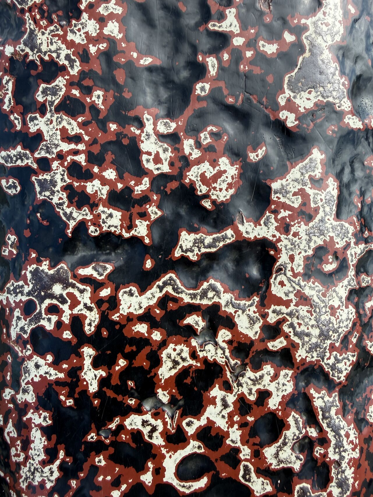 a close-up of peeling black and red paint on weathered metal, forming an abstract pattern
