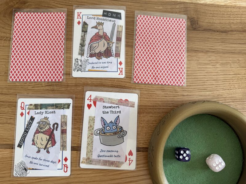 four hand-drawn poker cards laid out on a wooden table, including a king depicting Lord Honktimus the goose and a four of hearts showing Stewbert the Third, a small blue monster in a pot